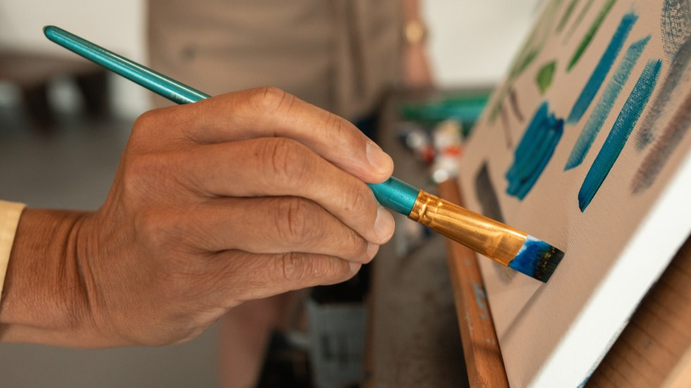 Een hand van iemand die met een kwast op het doek schildert