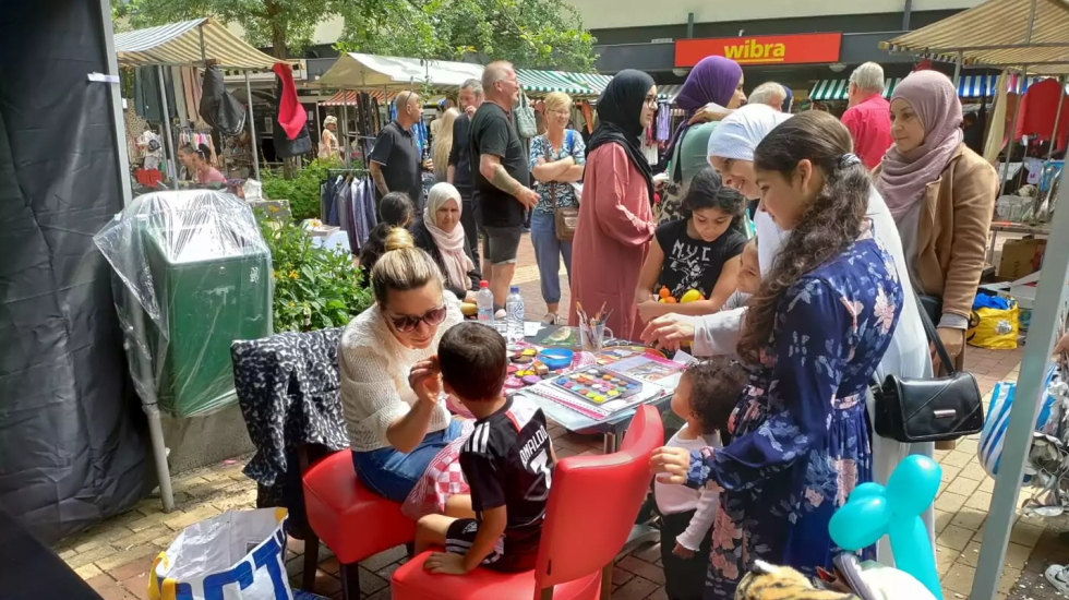 Een foto van de braderie: Bewoners staan rondom een kraampje op de markt