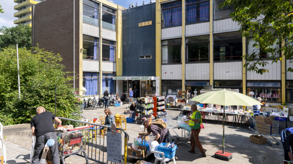 Het pleintje voor de Weggeefwinkel en drie mensen die tussen de uitgestalde spullen kijken