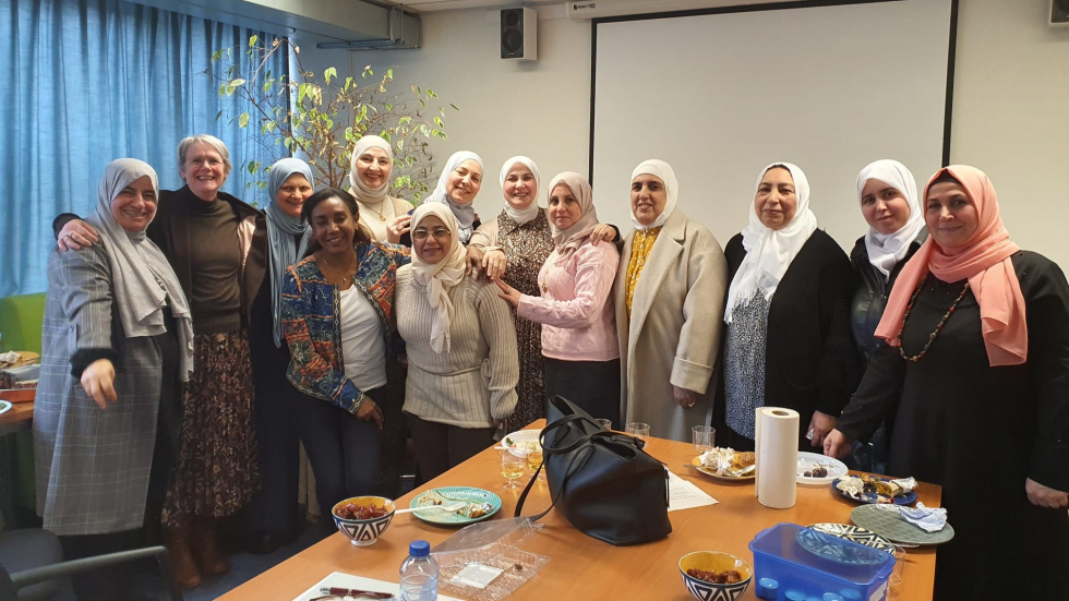 Een groepsfoto van 13 vrouwen tijdens een bijeenkomst, ze kijken in de camera en lachen