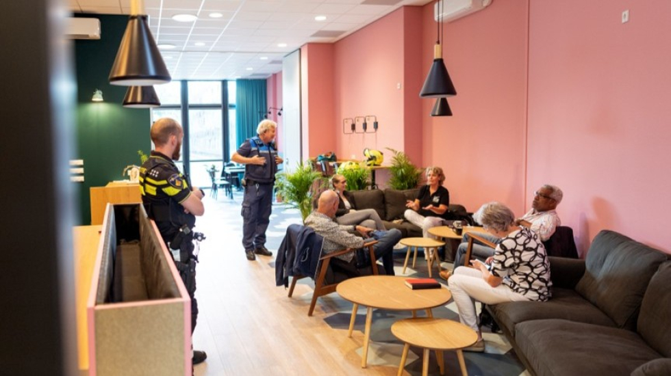 Foto van wijkcentrum 't Volle Hof met twee wijkagenten en een groepje van vijf bewoners die in gesprek zijn met elkaar