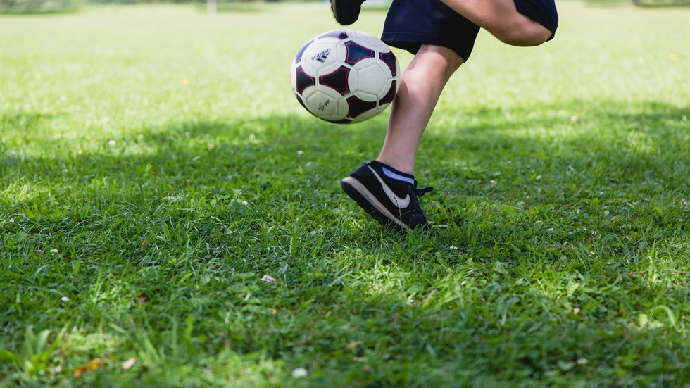 Een jongetje die een voetbal in de lucht trapt op een grasveldje. Je ziet alleen de benen van het jongetje.