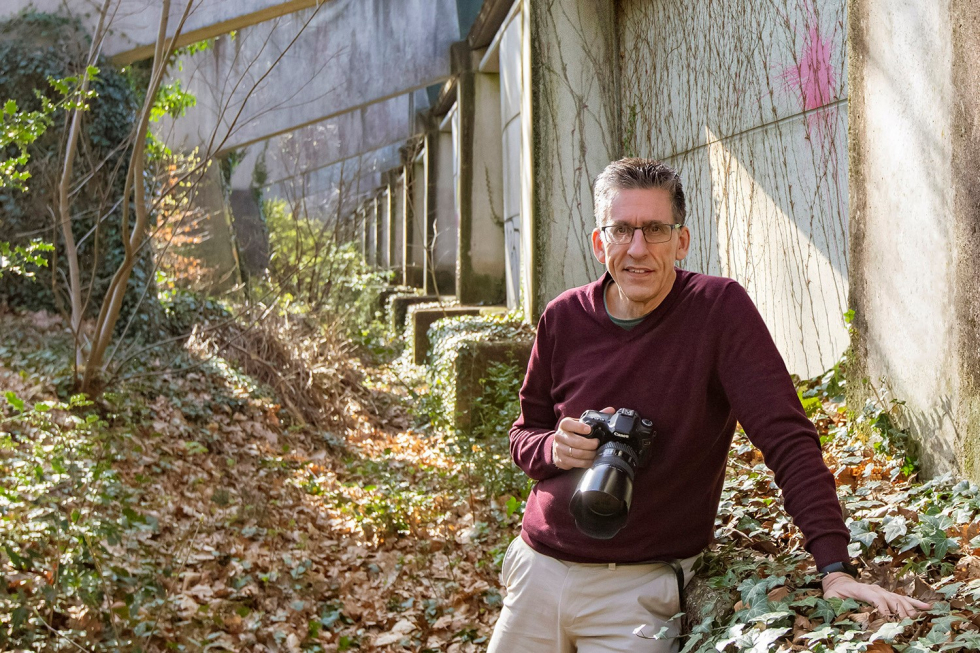 Fotograaf Fred Manschot bij de geluidswal, met een camera in zijn hand