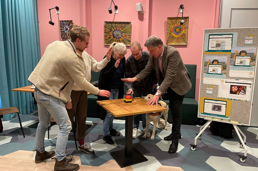Programmamanager Hans Goorhuis drukt samen met betrokken bewoners op de rode knop in 't Volle Hof. Ook is er een paneel te zien, waarop verschillende afbeeldingen van 't Volle Hof worden getoond. 