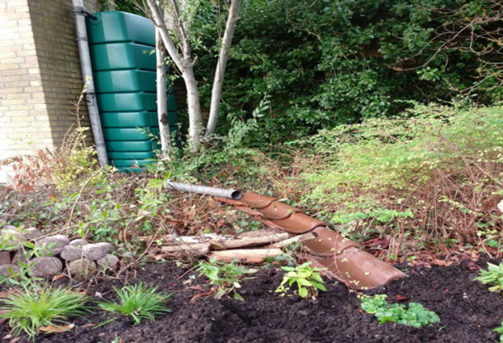 Een afgekoppelde regenpijp die in de tuin verlengd is met oude dakpannen
