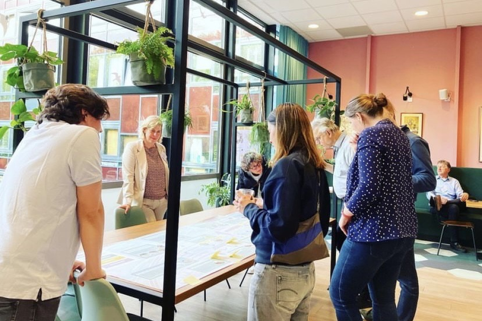 Bewoners die hun mening en ideeën delen tijdens de eerste inloopavond in 't Volle Hof. Ze staan om een tafel waarop tekeningen liggen.