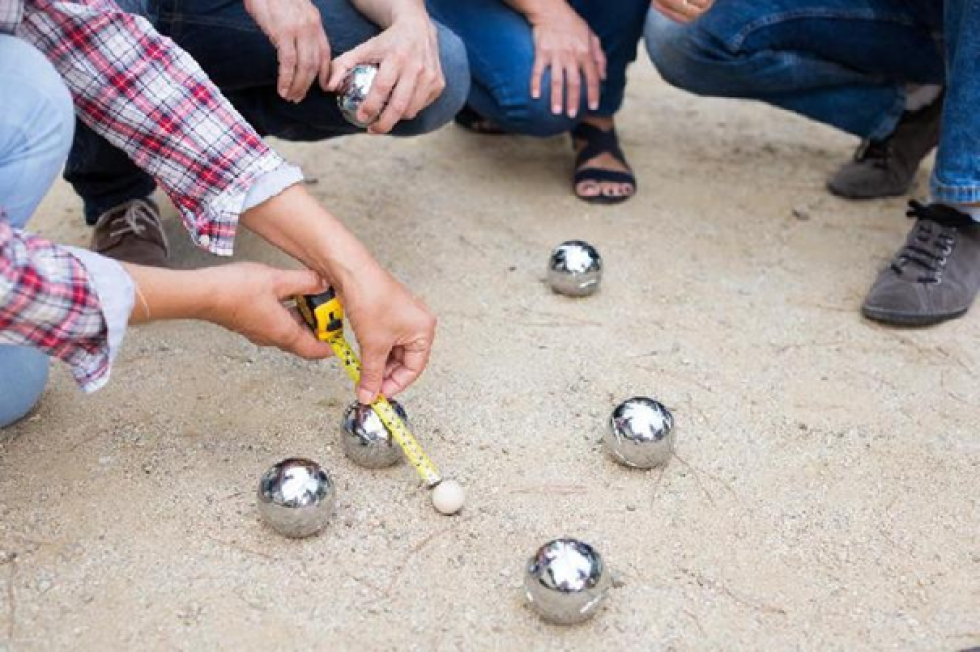 Mensen die met een meetlint de afstand tussen de Jeu de Boules ballen aan het opmeten zijn. 