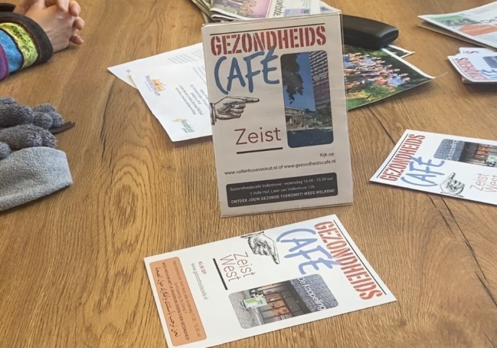 Flyers van het Gezondheidscafé op tafel. Op de flyer staat het logo van Het Gezondheidscafé met een foto van de wijk Vollenhove. 