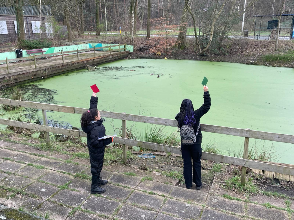 Twee kinderen bij het slootje achter de L-flat en Park Vollenhove. Een kind steekt een rode kaart op en het andere kind een groene kaart. 
