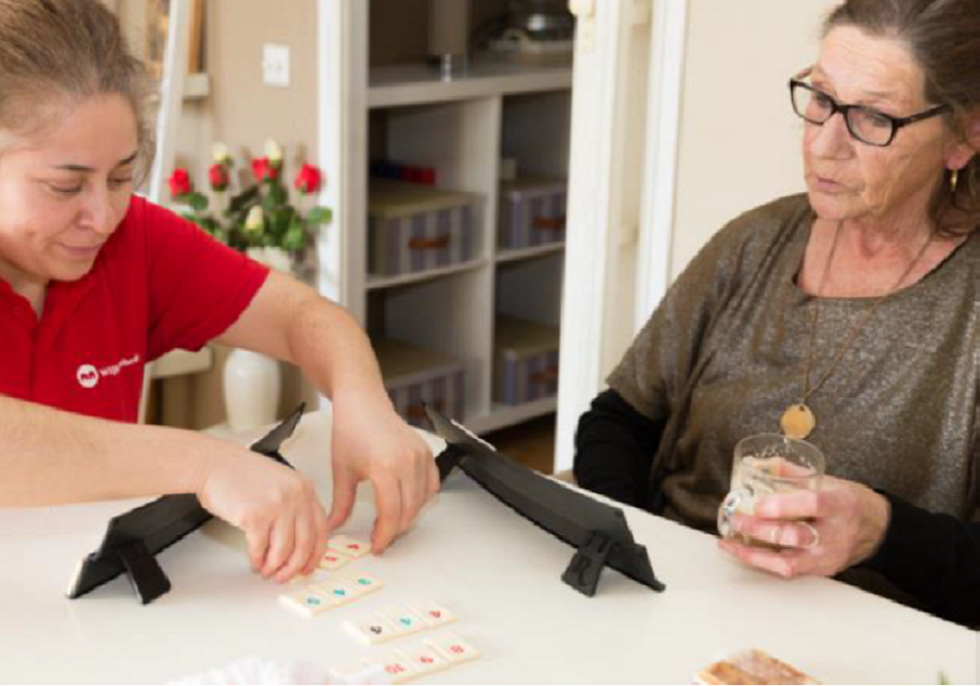 Een vrouw van het WijkLeerbedrijf die samen met een andere vrouw een spelletje speelt. 