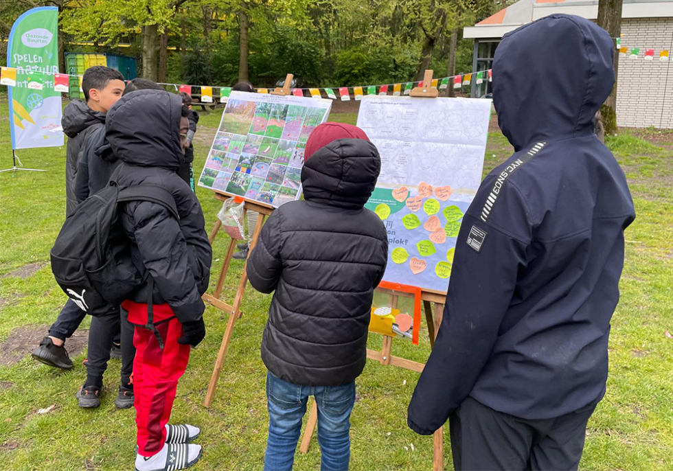 Een aantal kinderen die in het park staan en naar verschillende ontwerpen en schetsen kijken van het park kijken.