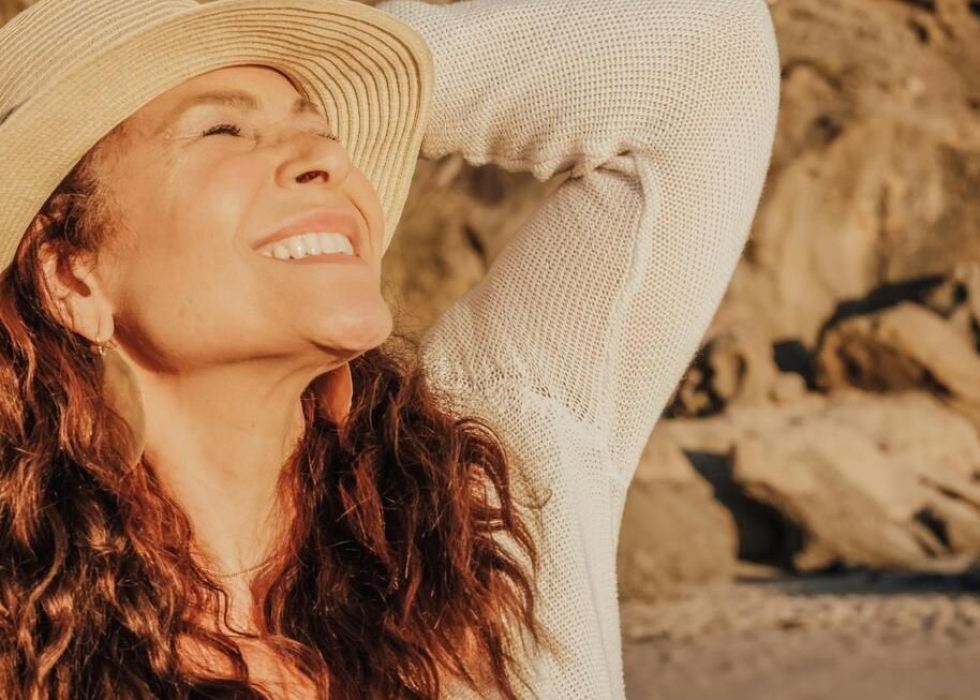 Een foto van een vrouw met een zomerhoed op terwijl ze lachend richting de zon kijkt. 