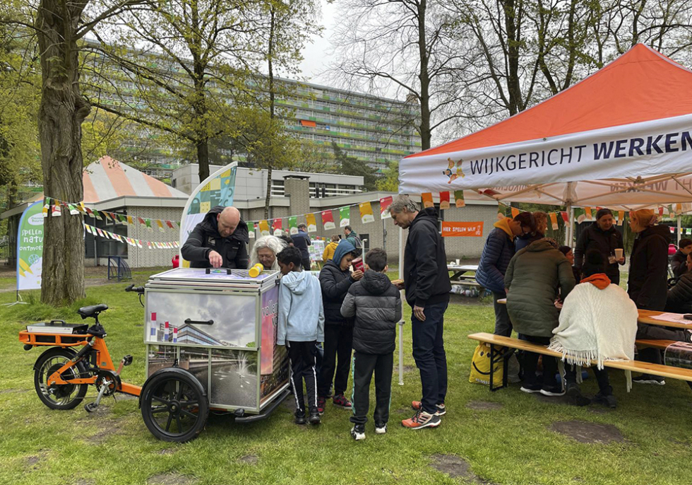 In Park Vollenhove staan een aantal kinderen en volwassenen rond de Soepkar. Ook staat er een partytent waar mensen onder zitten. Op de partytent staat de slogan: wijkgericht werken.
