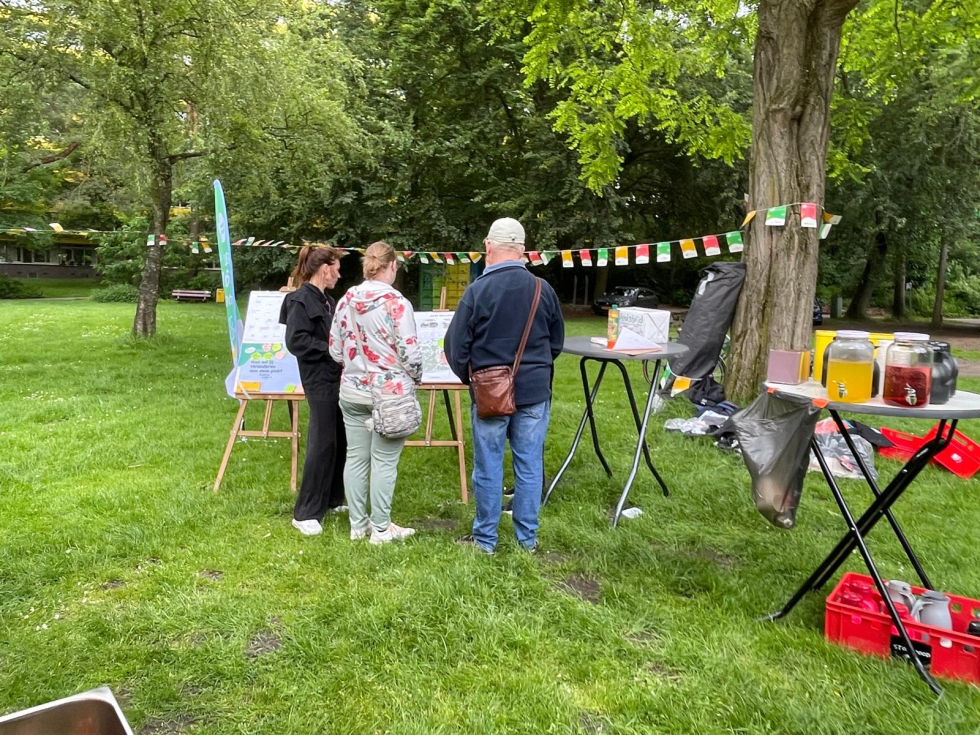Mensen in het park kijken naar een bord met het ontwerp en krijgen hier uitleg over. 
