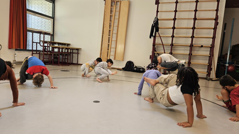Kinderen doen een dansworkshop waarbij ze aan het breakdancen zijn in een gymzaal