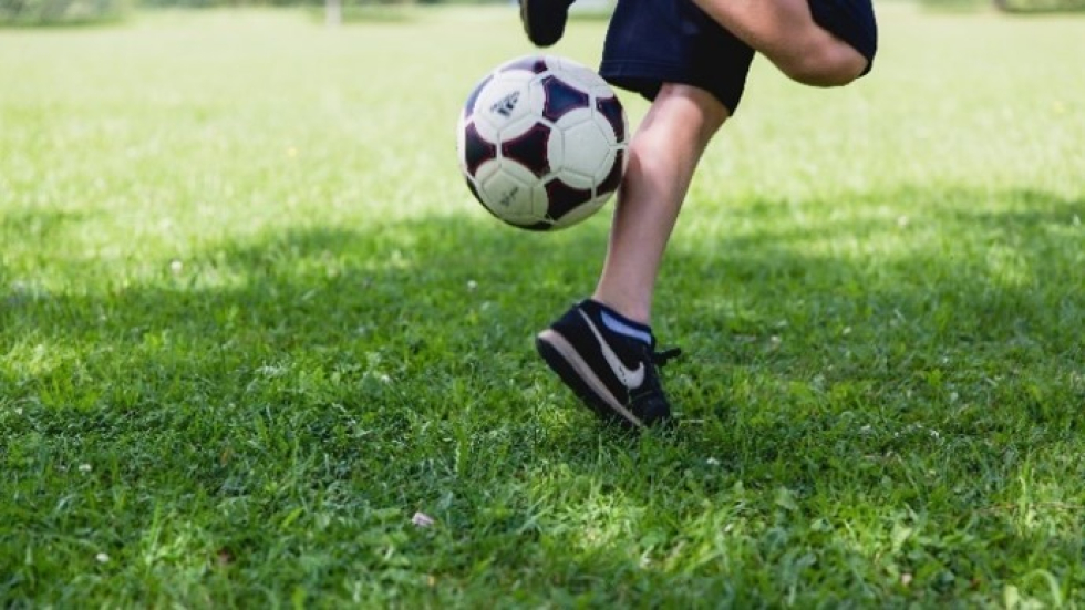 Foto van een kind op een grasveld die met een voetbal speelt