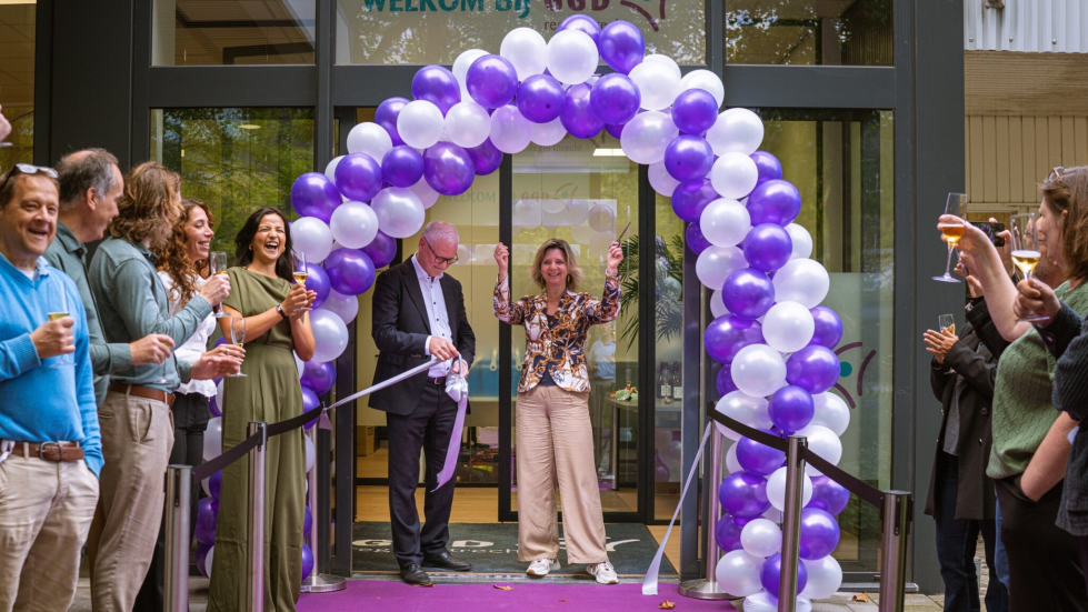 Foto van de opening voor de ingang: met een boog van balonnen en lachende, proostende mensen